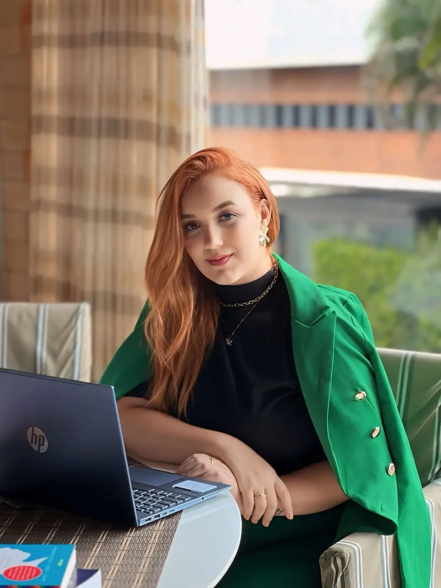Thalita Macedo sentada, de blazer verde, ao lado de um notebook